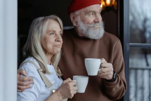 elderly couple holding cups while looking out a window