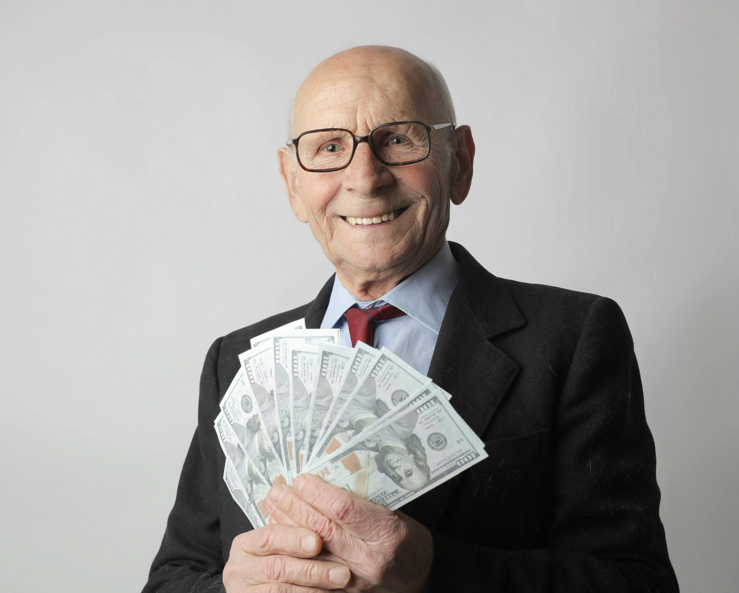 smiling older man in a suit holding a spread of dollar bills